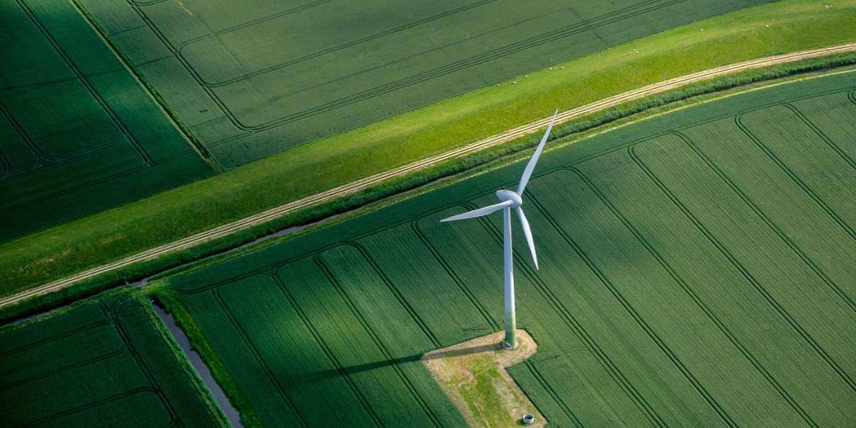 Aerial view of a wind turbine surrounded by green crop fields and a narrow road