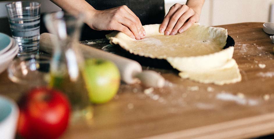 A table with glass apples and person preparing pie crust on a kitchen counter.