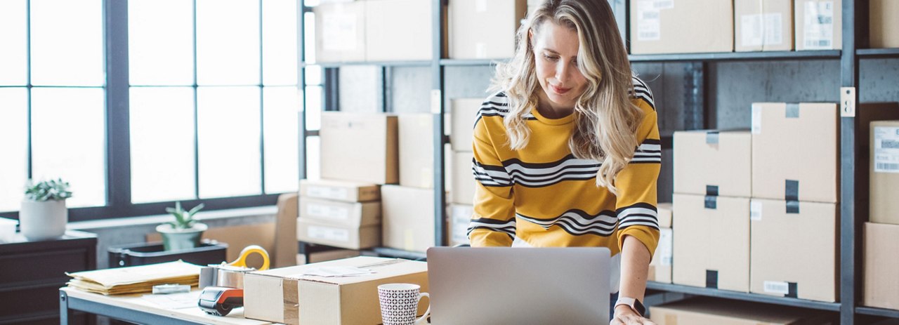 a women in a yellow shirt with black and white strips on it working on a laptop around ebay boxes