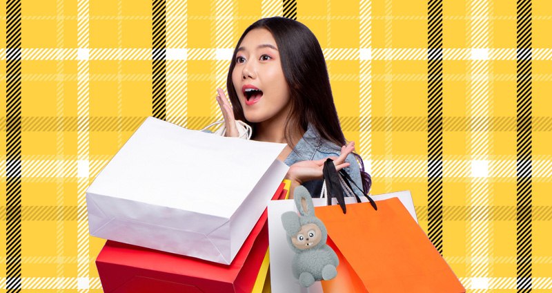 Person holding multiple colorful shopping bags against a yellow plaid background.
