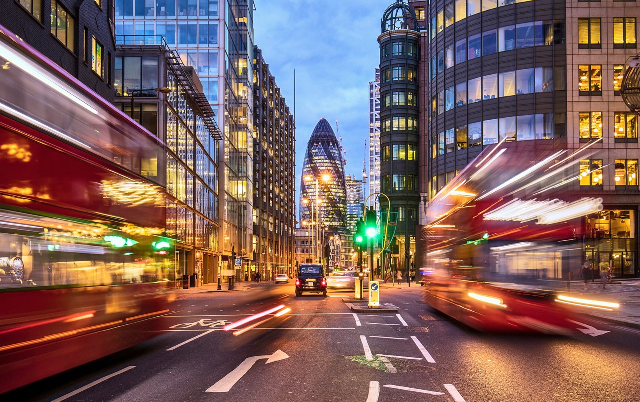 Financial district in London at dusk with buses driving through.