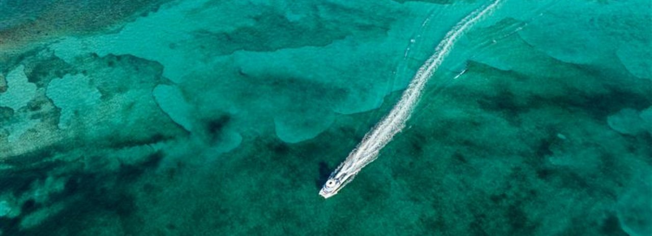 Aerial view of a boat cruising through clear turquoise waters, leaving a white wake behind.