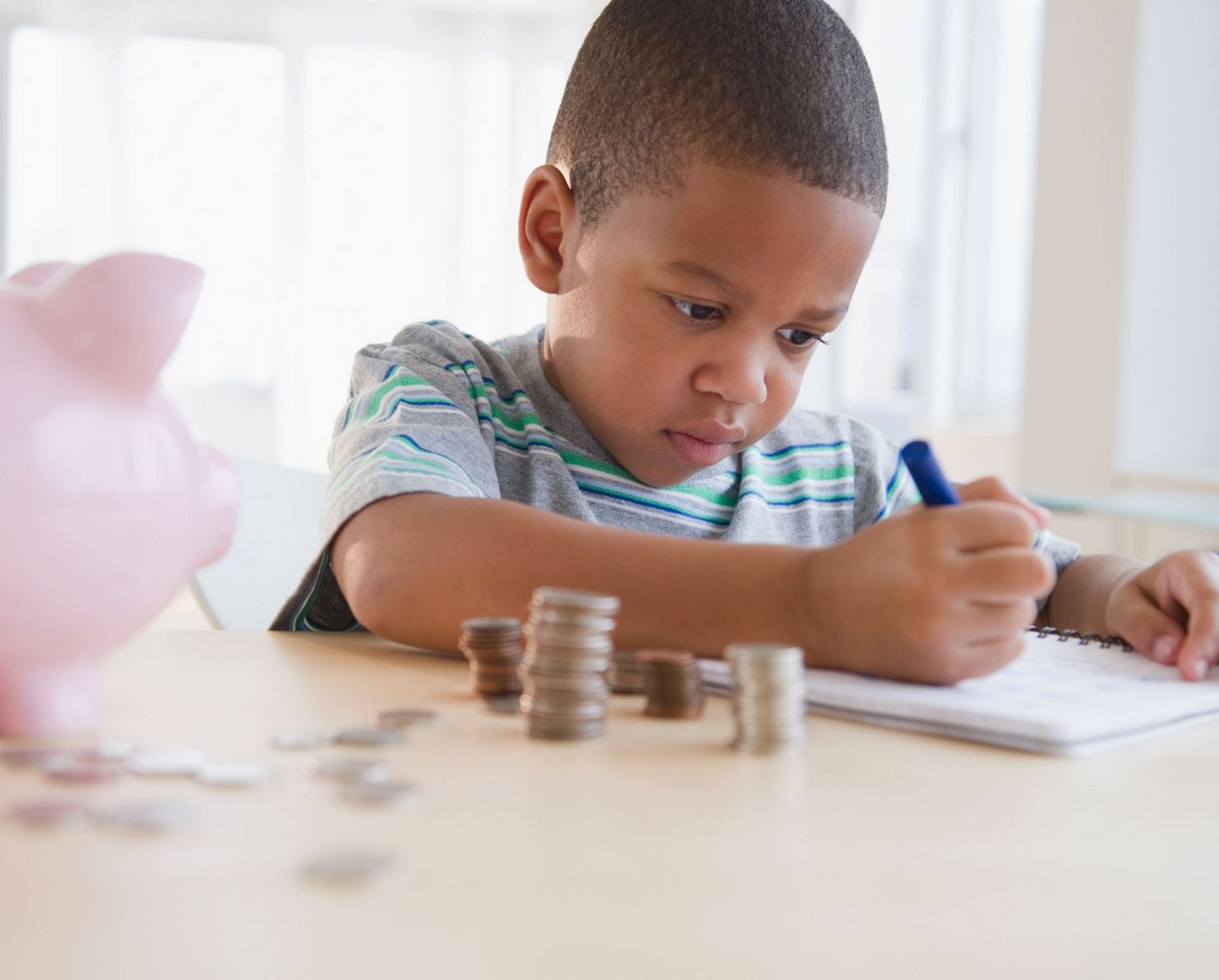 kid making notes sitting with money and piggy bank