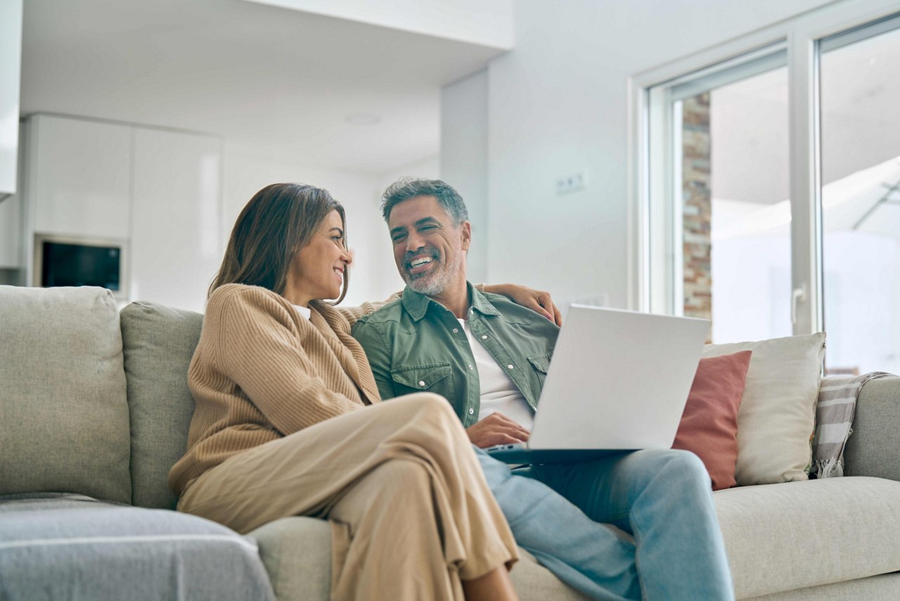 Happy mature couple using laptop relaxing on sofa in living room. Candid shot.