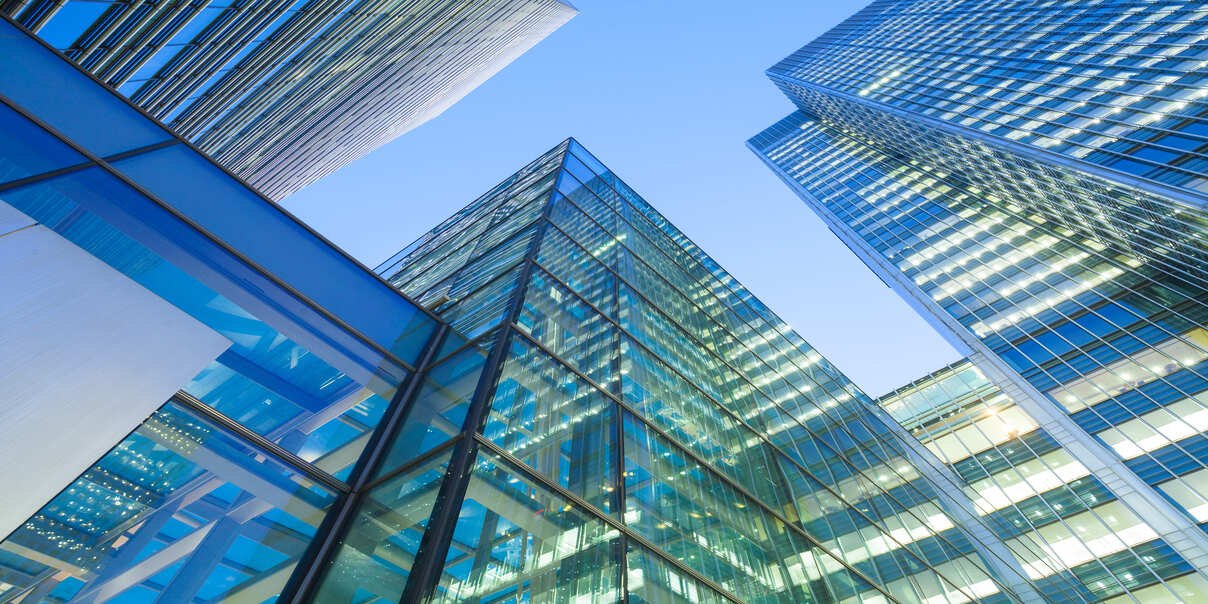Tall modern glass skyscrapers reflecting light against a clear blue sky, viewed from a low angle.