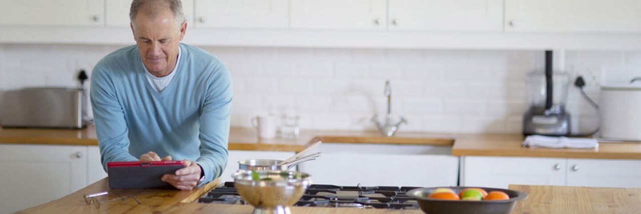 Man leaning on the kitchen counter while scrolling on his tablet