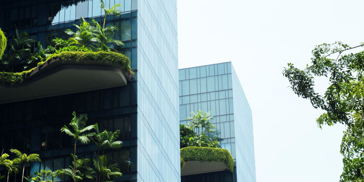 Modern high-rise buildings with glass facades and multiple levels of greenery, including trees and plants on terraces and balconies, showcasing sustainable urban architecture.