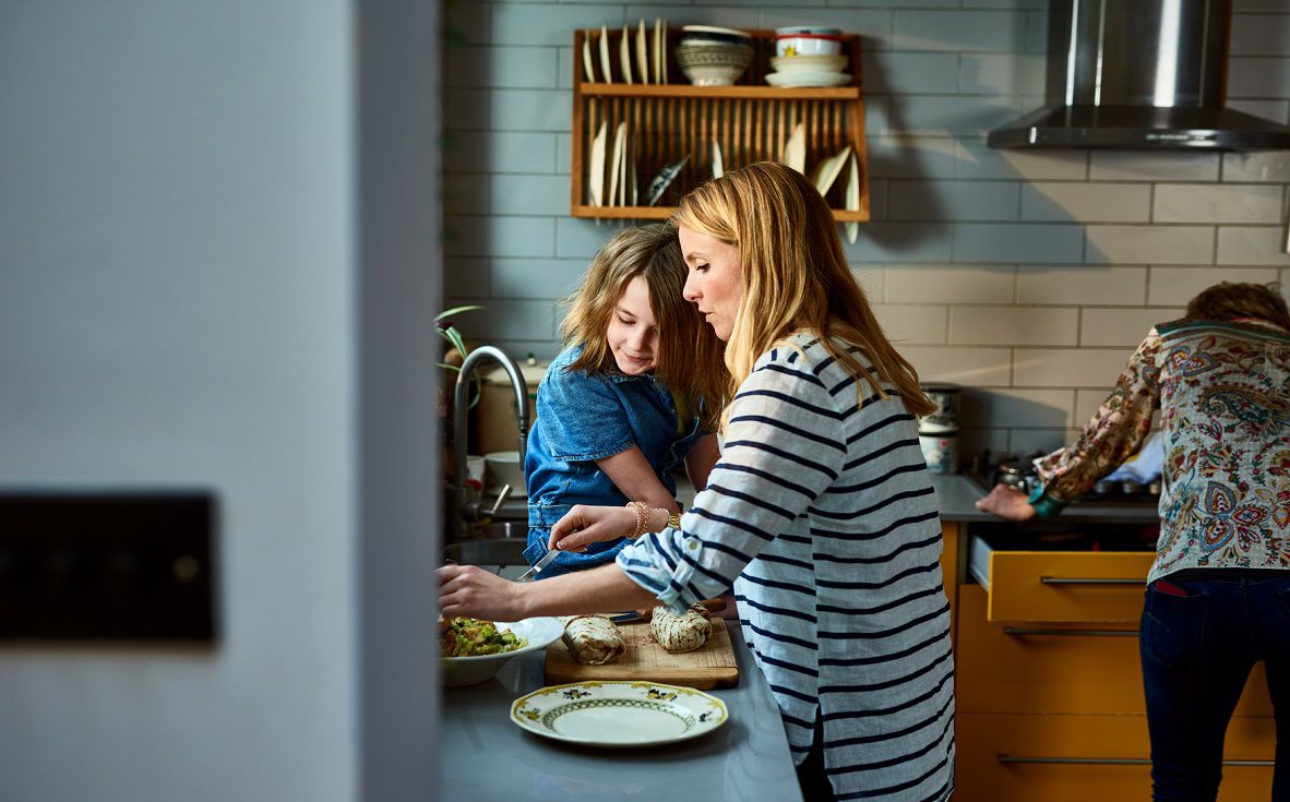 Side view of mother preparing food, daughter sitting on kitchen kitchen counter