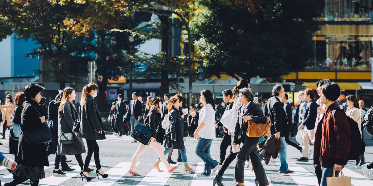 Crowd of people crossing a city street at a crosswalk on a sunny day