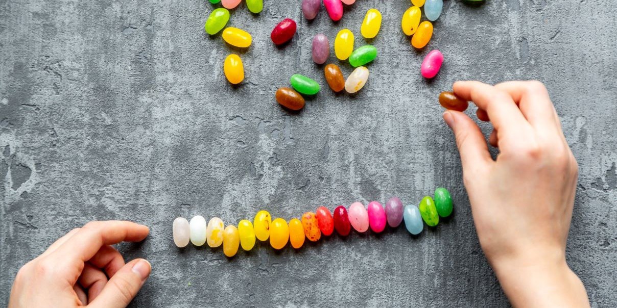 A person's hands are arranging colourful jellybeans in a row on a grey surface
