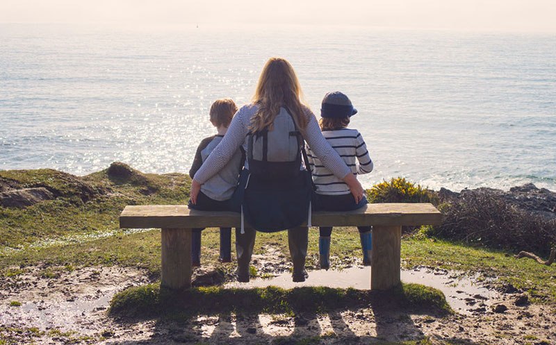 Women with two children sitting on a bench looking at the sea