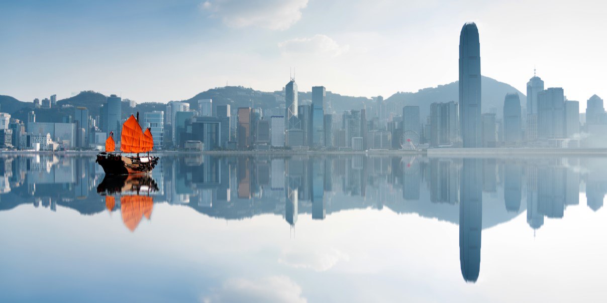 A sailboat glides through the water with the stunning Hong Kong skyline visible in the background.