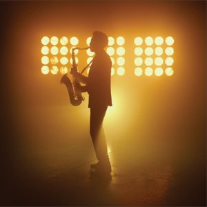 A saxophonist silhouette playing in front of a bank of lights