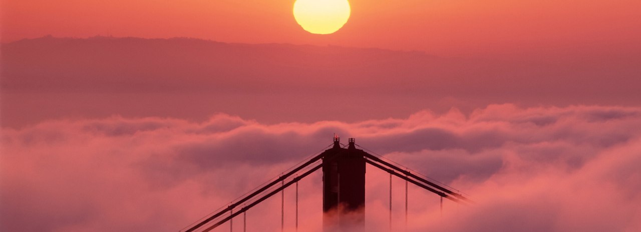 The sun glows warmly in the sky, painting the clouds and atmosphere in soft shades of orange and pink.