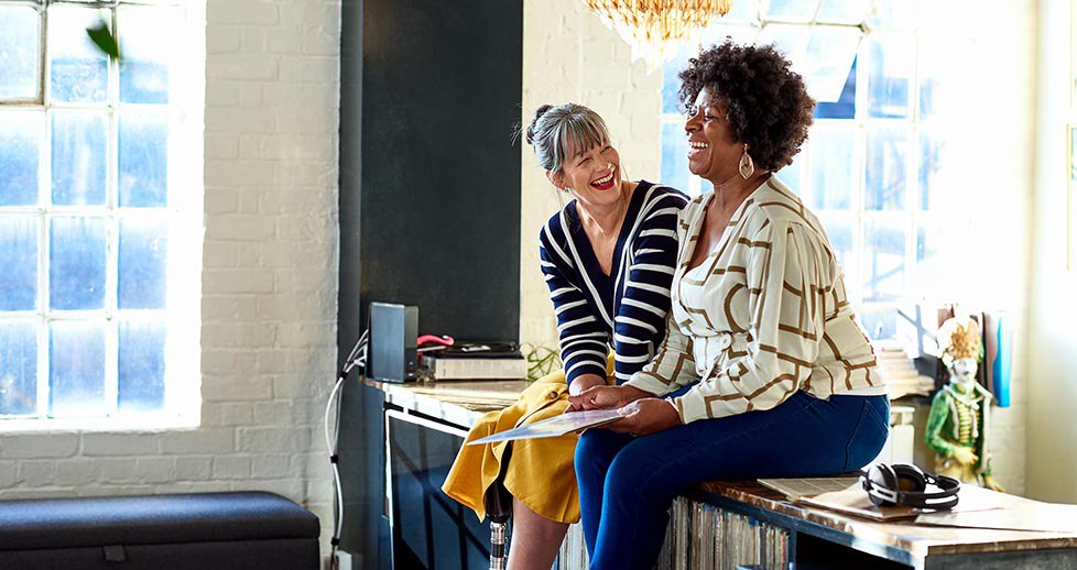 Two female friends sitting on sideboard and smiling, friendship, fun, memories, wellbeing