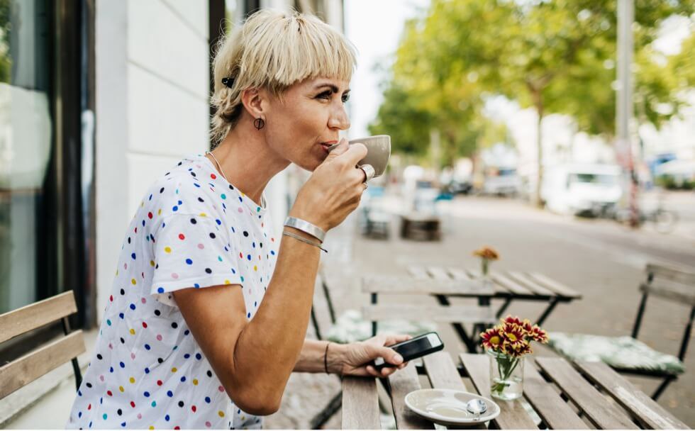 Woman sitting outside a cafe on a sunny day drinking out of a mug