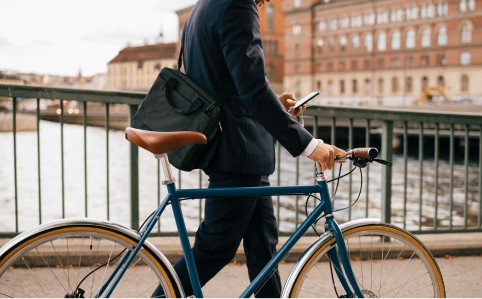 A person in a dark suit walking alongside their bike while scrolling on their phone