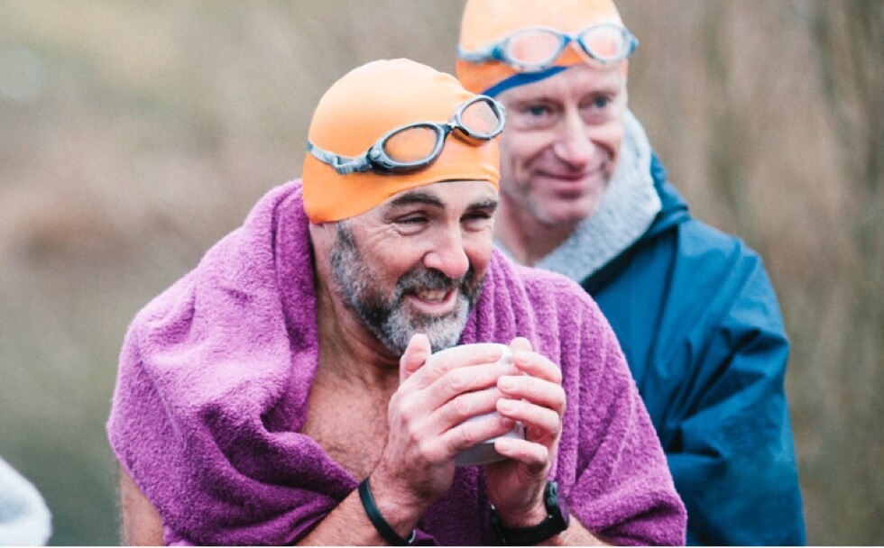2 man wearing swiming gears and 1 shivering holding cup in hand