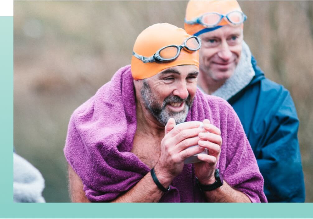 2 Man wearing swimming gears with towel on shoulder shivering holding a cup