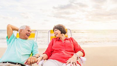 two people sitting on the beach looking at each other and smiling