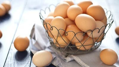 A woven basket filled with various eggs resting on a rustic wooden table, showcasing natural textures and colors.