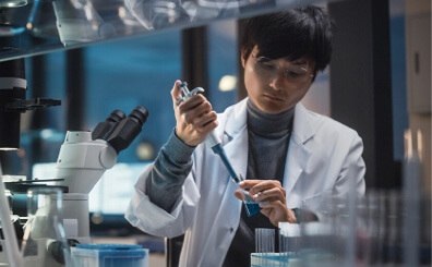 A young Asian man in a lab coat is focused on his work, examining materials in a laboratory setting