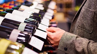 A man examines various wine bottles on display in a retail store, contemplating his selection.