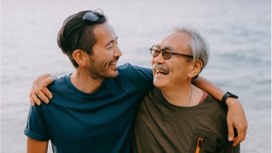 Two men hug on the beach, capturing a heartfelt moment against the tranquil setting of sand and sea.