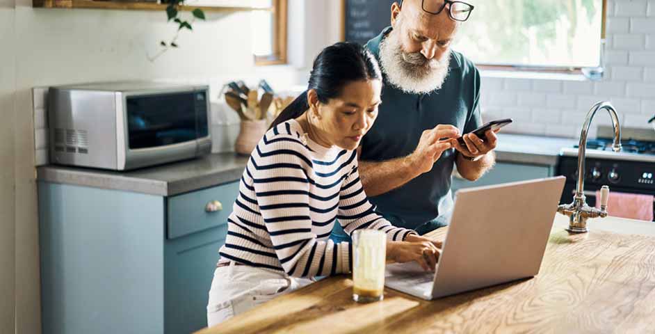 Man and woman working on a laptop together in a kitchen setting.