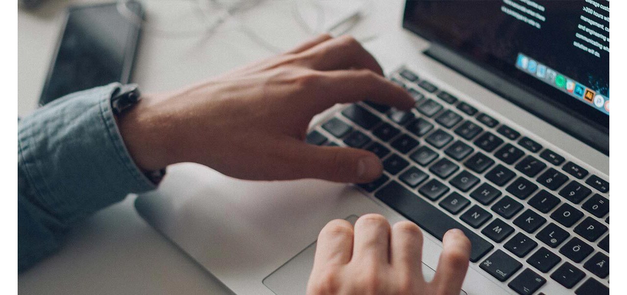 The hands of a person in a long sleeve shirt shown typing on a Macbook keyboard