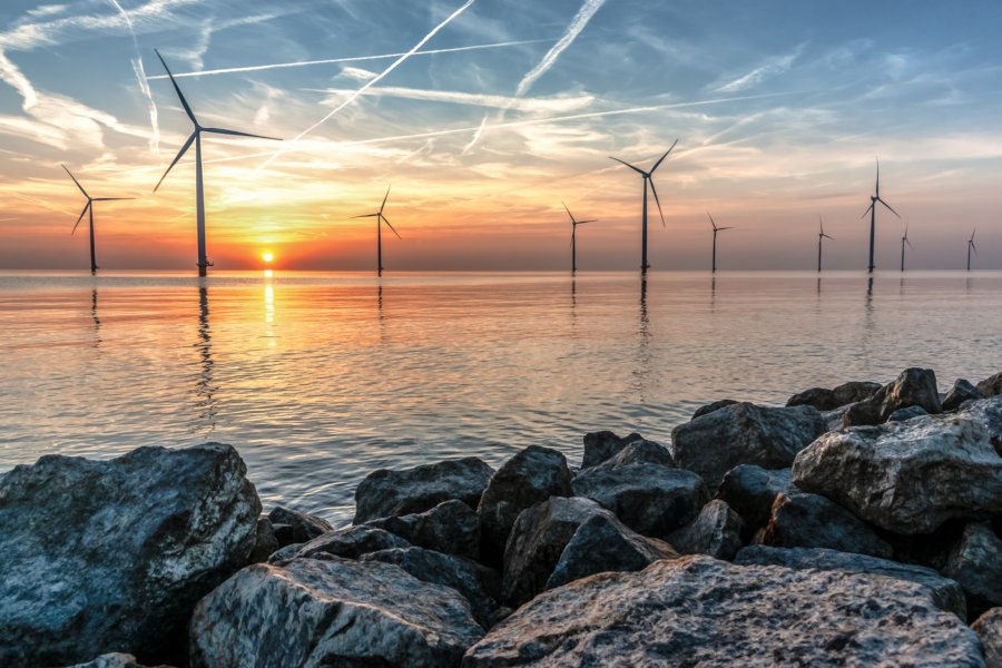 Romantic atmospheric sunset over the largest lake in the Netherlands (Ijsselmeer). Modern windmills stand in the water in a wind farm with a view from the dike and the basalt blocks of water protection.