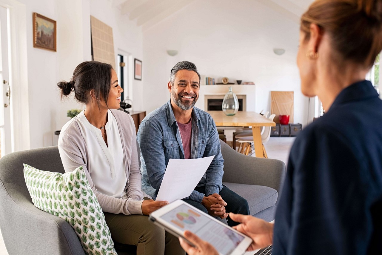 Happy mature couple discussing investments with financial broker during meeting at home. Happy middle eastern man and hispanic woman discussing about financial planning with consultant at home. Financial consultant presenting new investment plan to smiling mature couple at home. 